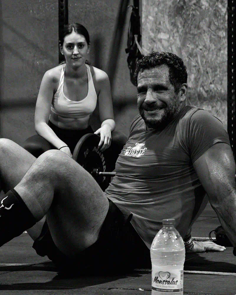 Socio sentado en el suelo tras el WOD, sonriendo a cámara junto a una compañera