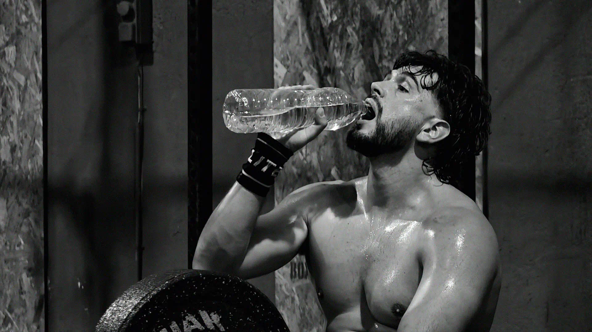 Atleta sin camiseta bebiendo agua junto a la barra tras terminar el WOD